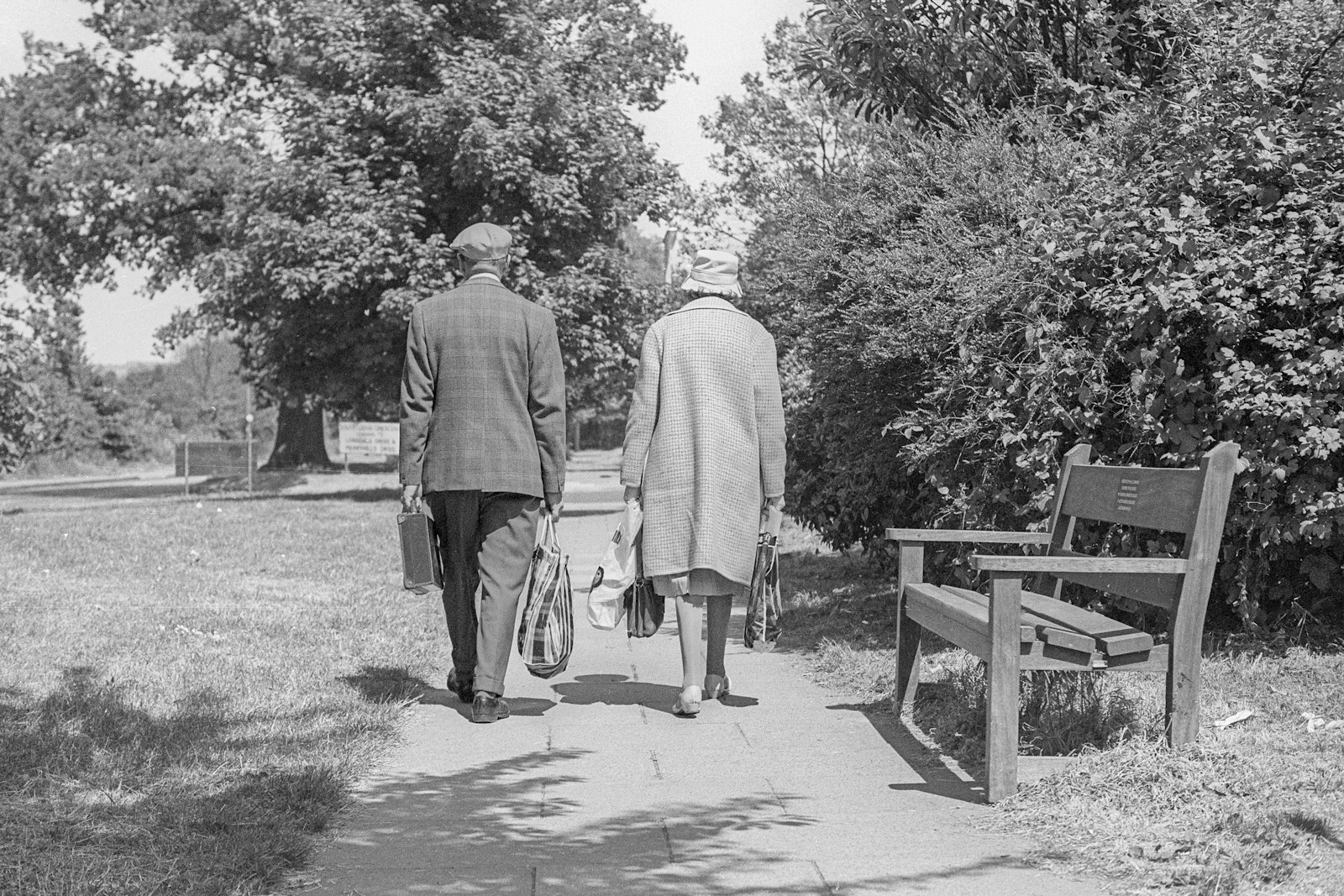 An older couple walking together along a tree-lined park path
